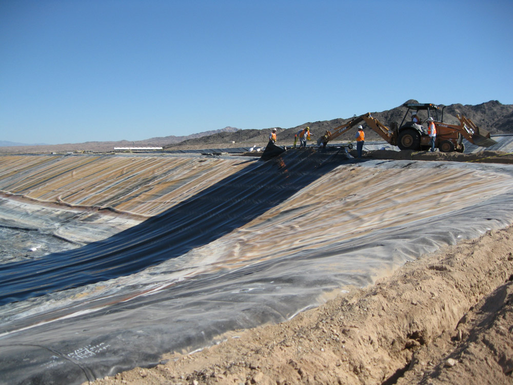 Several Alisto team members laboring in a deep trench, wearing hard hats and reflective vests, surrounded by construction equipment
