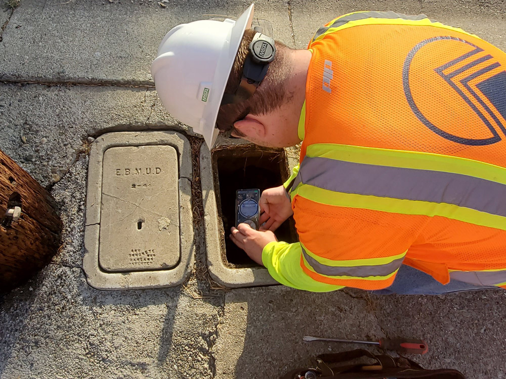 A man in an orange vest and hard hat repairing a sewer pipe